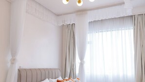 A bedroom with a bed, bedside table, curtains, and a chandelier. - Koriwo Haven- Your Home Away From Home in Nairobi (Syokimau)