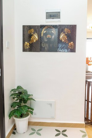 A wall-mounted artwork of golden jewelry pieces, a potted plant, and a thermostat.