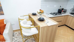 A compact kitchen with a central island, a bar stool, a white sofa with an orange throw, and a patterned rug. - Koriwo Haven- Your Home Away From Home in Nairobi (Syokimau)