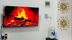 Un televisore montato su una parete bianca mostra un camino, un dispenser d'acqua e decorazioni murali.