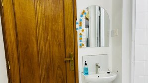 Un bagno con una porta in legno, un lavandino bianco, uno specchio e una doccia.