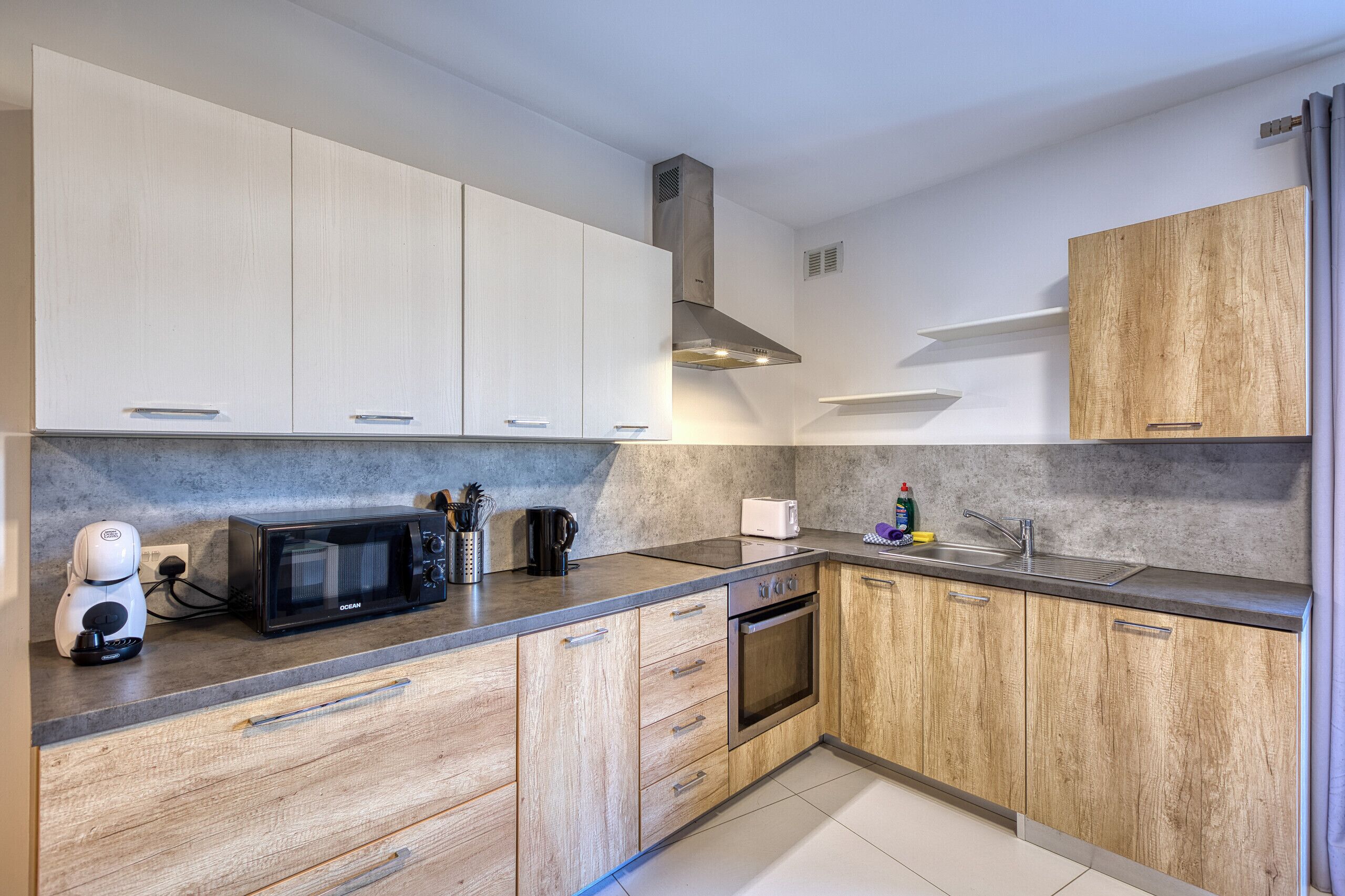 A modern kitchen with a microwave, toaster, and coffee maker on the counter, wooden cabinets, and a stainless steel range hood.