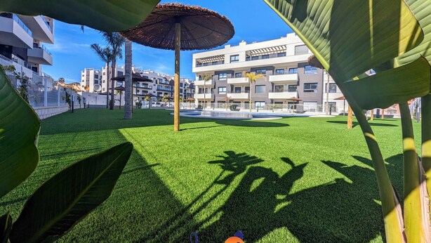 A courtyard with artificial grass, a central umbrella, and modern buildings in the background. - Chic 2 bedroom Apartment with Comunal Pool VM75 (Villamartín)