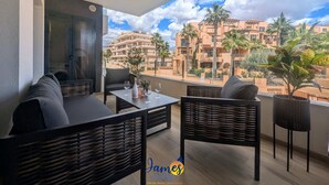A balcony with wicker furniture, a table with a bottle and glasses, and a view of a residential area with palm trees and buildings. - Chic 2 bedroom Apartment with Comunal Pool VM75 (Villamartín)