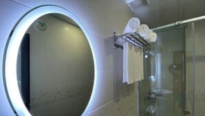 Une salle de bain avec un miroir rond, une cabine de douche en verre et un porte-serviettes avec des serviettes.