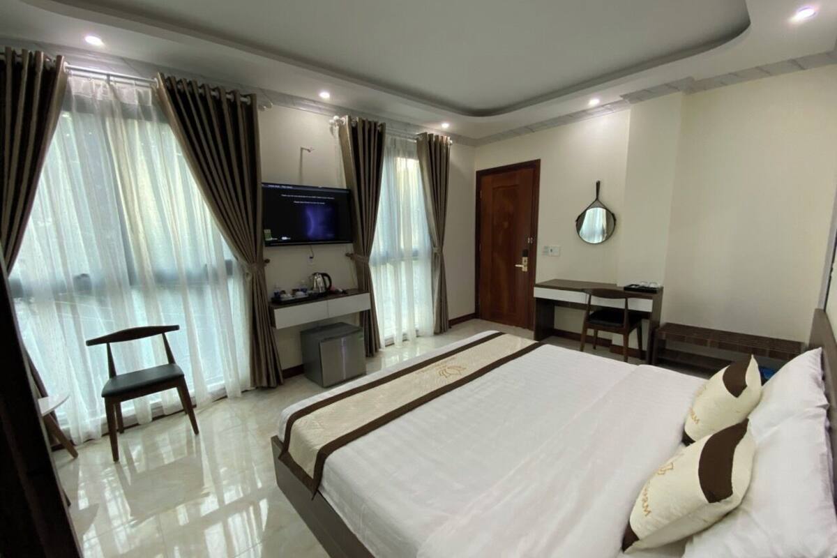 A hotel room with a large bed, a desk, a chair, a TV, and a mirror.