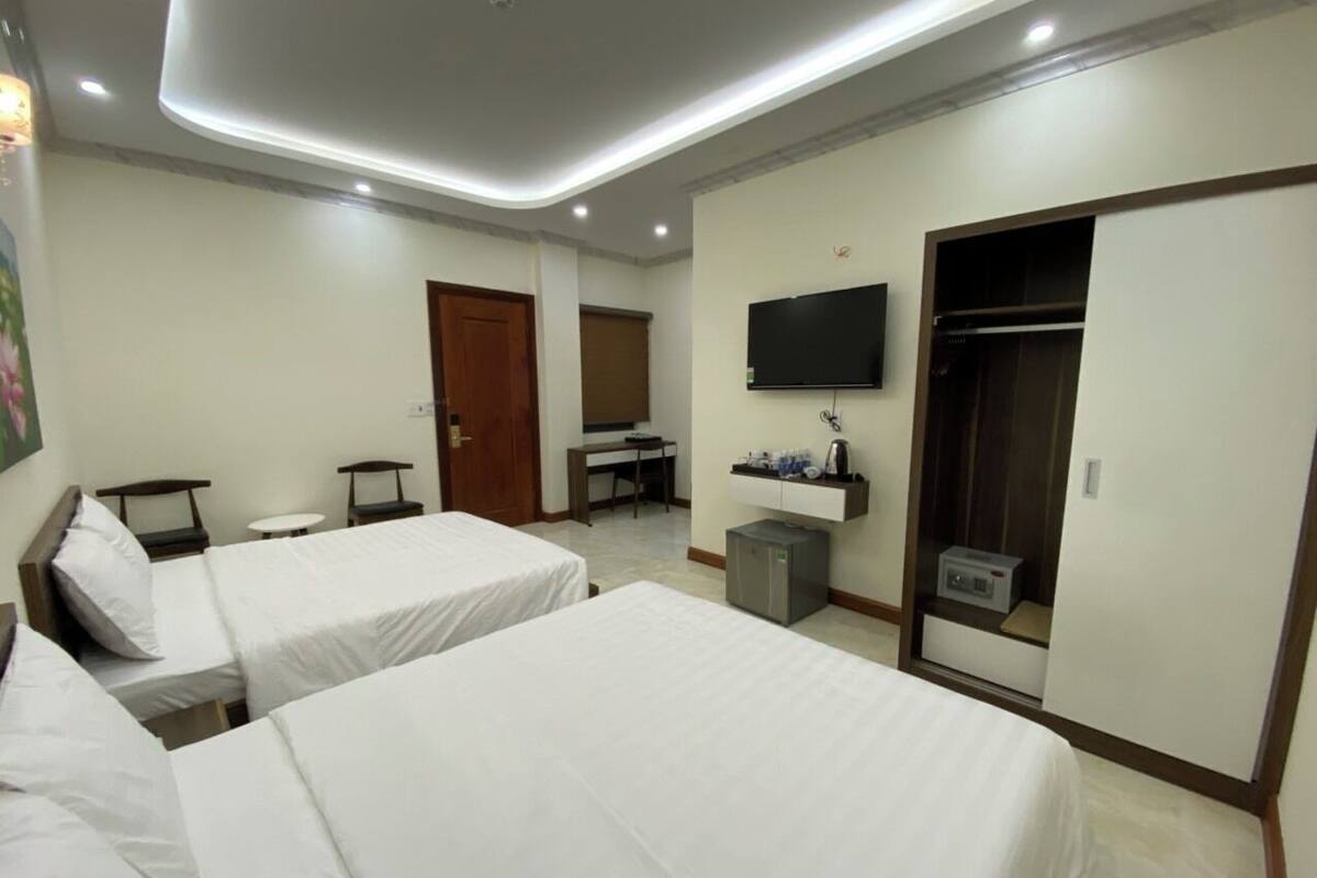 A hotel room with two beds, a desk, a TV, a wardrobe, and a small table.