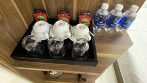 Un plateau avec des sachets de thé et de café, des tasses et des bouteilles d’eau.