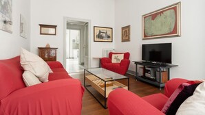 Una sala de estar con sofás rojos, una mesa de centro de vidrio, un televisor y obras de arte en las paredes.