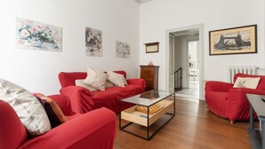 Sala de estar con sofás rojos, una mesa de centro de vidrio y cuadros en la pared.
