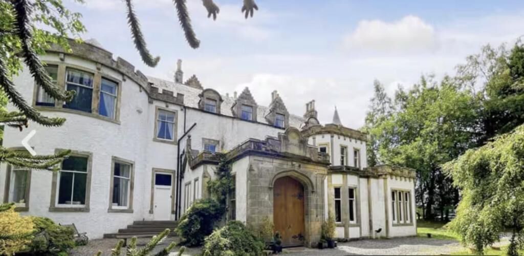 A historic building with a central arched entrance, multiple windows, and a stone facade.