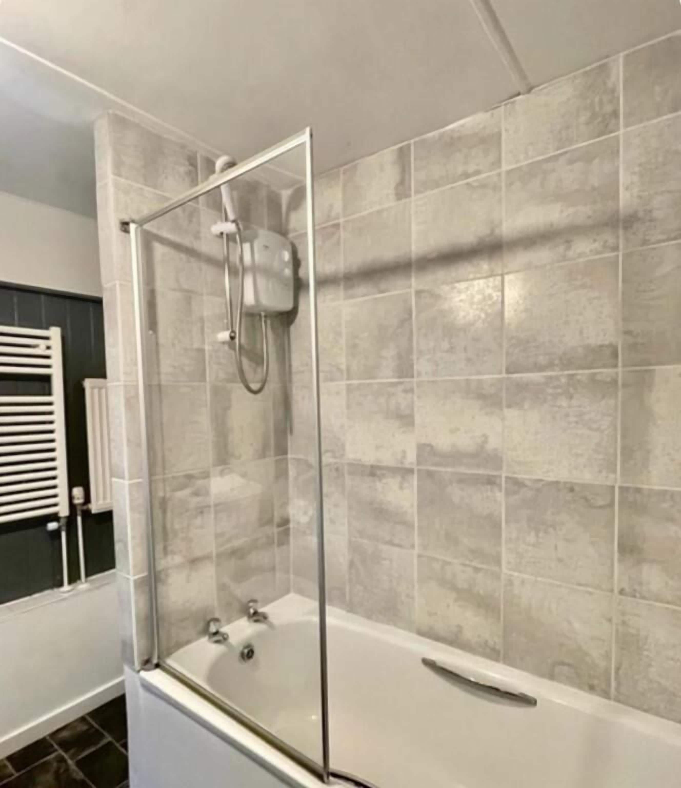 Une salle de bain moderne avec une douche à parois de verre, une baignoire blanche et des murs recouverts de carreaux gris.
