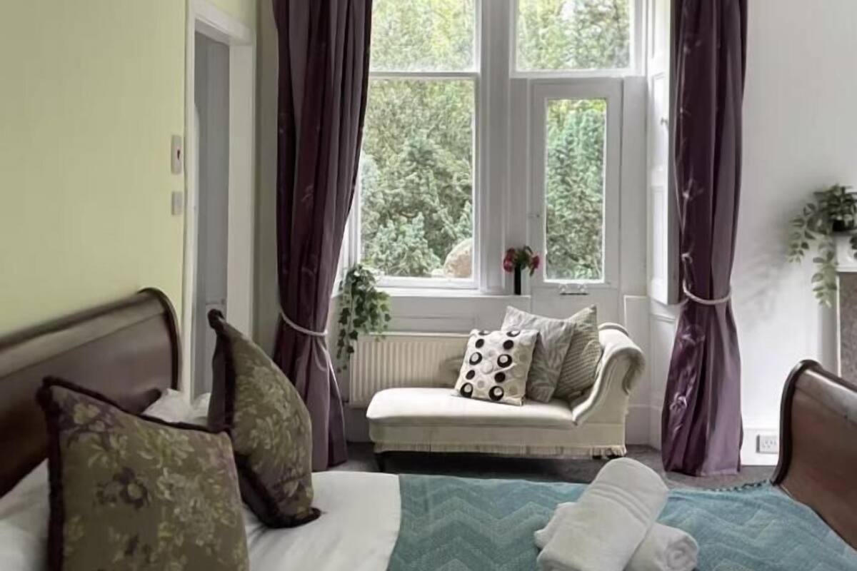 A bedroom with a bed, a window with curtains, a radiator, and a plant.