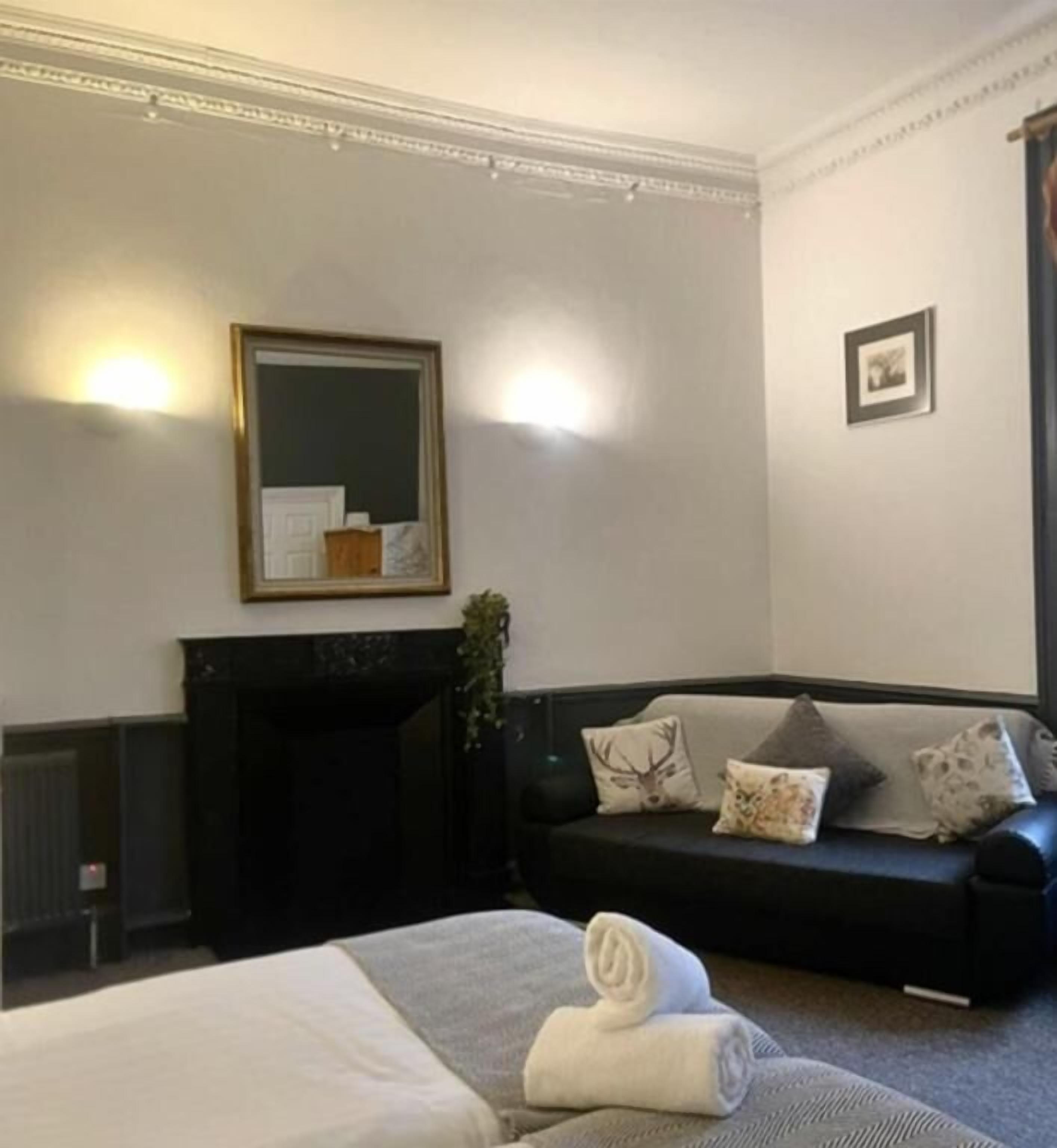 A hotel room with a bed, a black sofa, a fireplace, and a mirror on the wall.