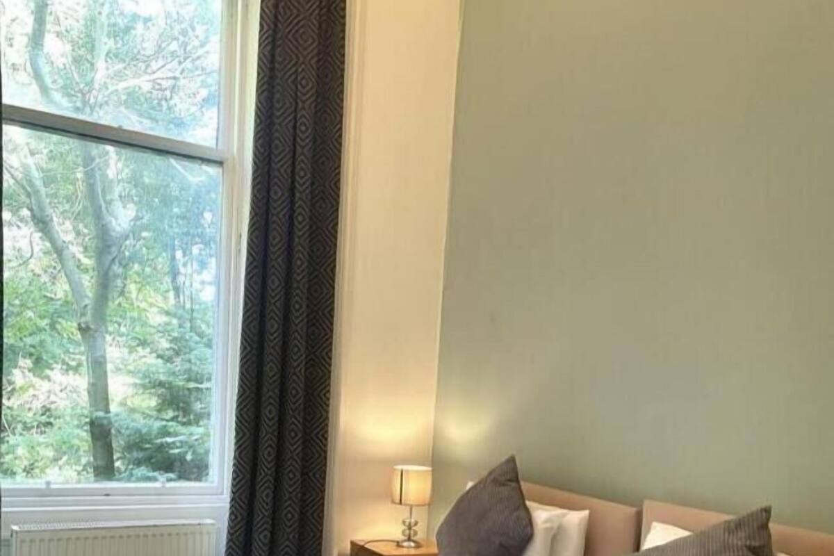 A hotel room with two beds, a window with a view of trees, and a nightstand with a lamp.