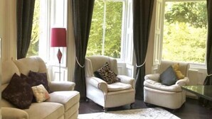 Une pièce dotée d’un plafond incurvé, de grandes fenêtres avec des rideaux foncés, de deux fauteuils avec des coussins et d’un lampadaire rouge.