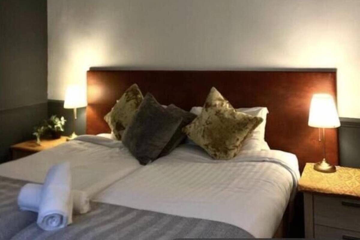 A hotel room with a neatly made bed, two bedside lamps, and a headboard.