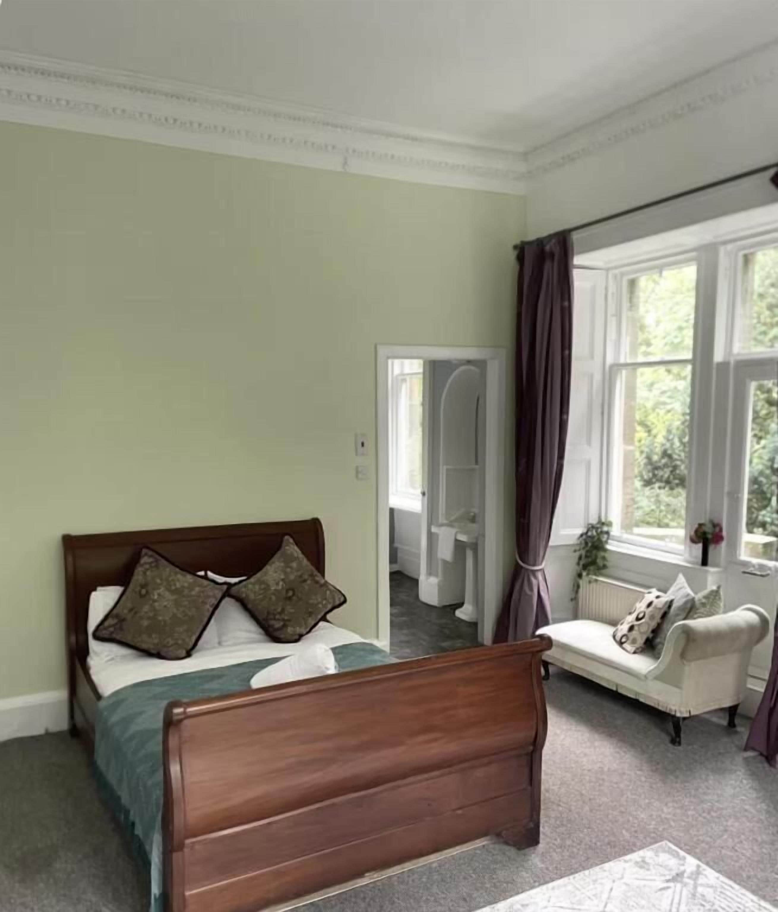 A bedroom with a wooden bed, a white sofa, and a window with curtains.