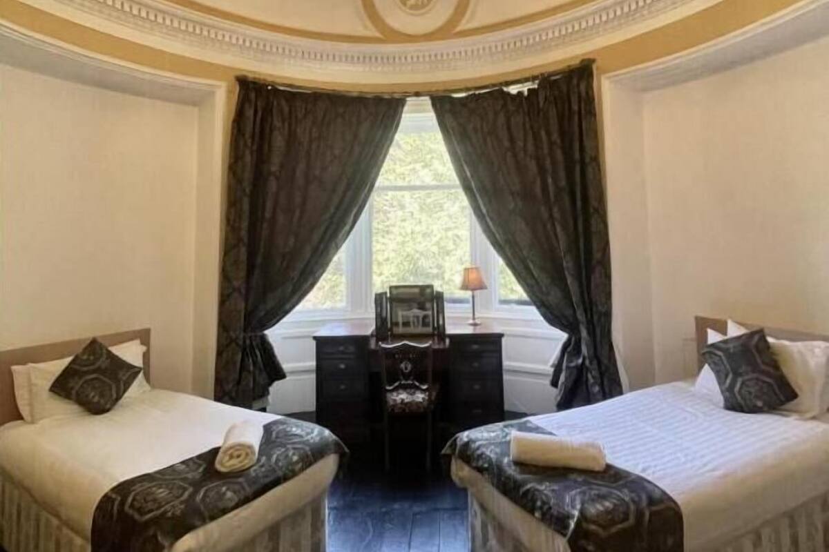 A room with two beds, a desk, and a window with curtains.