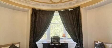 A room with two beds, a desk, and a window with curtains.