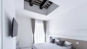 A modern bedroom with a skylight, a bed with pillows, a bedside table, and a mounted TV. - Alberti Apartments Historical Center Trapani (Trapani)