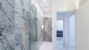 A modern bathroom with marble walls and a glass shower enclosure. - Alberti Apartments Historical Center Trapani (Trapani)