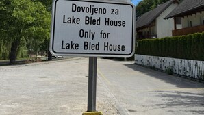 Señal de estacionamiento con fondo azul y un símbolo de 'P' blanco, indicando una zona de estacionamiento. Debajo, hay otra señal con texto en un idioma no inglés, que probablemente especifica normas o restricciones de estacionamiento.