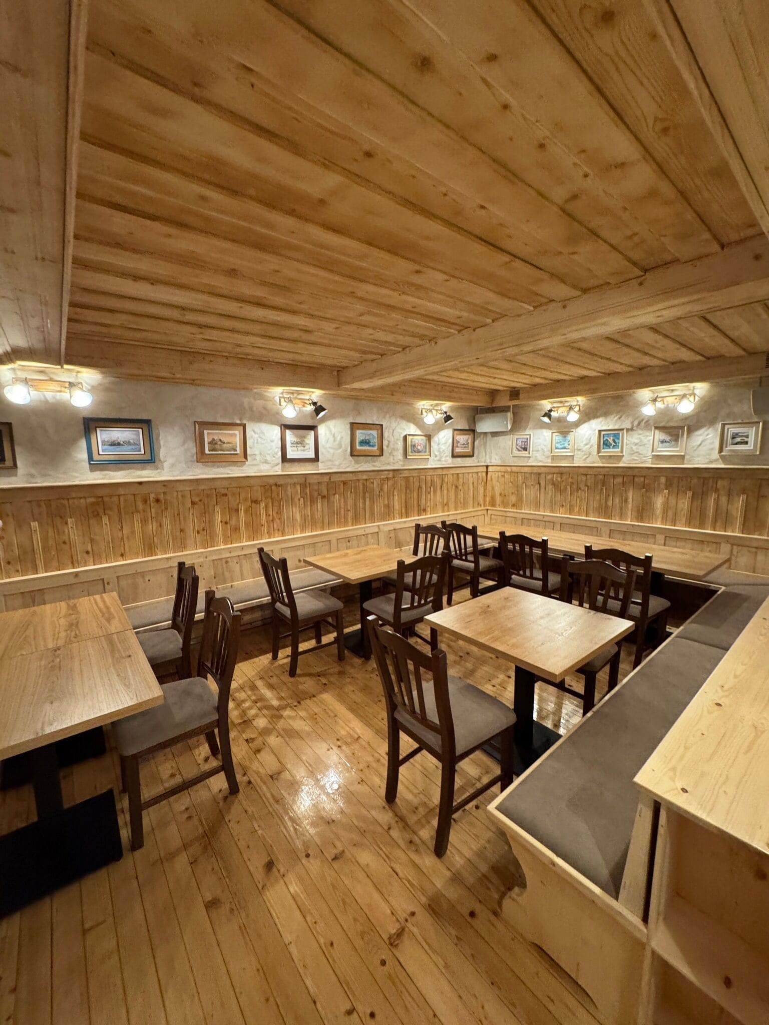 A restaurant with wooden tables and benches, framed pictures on the walls, and a wooden ceiling.