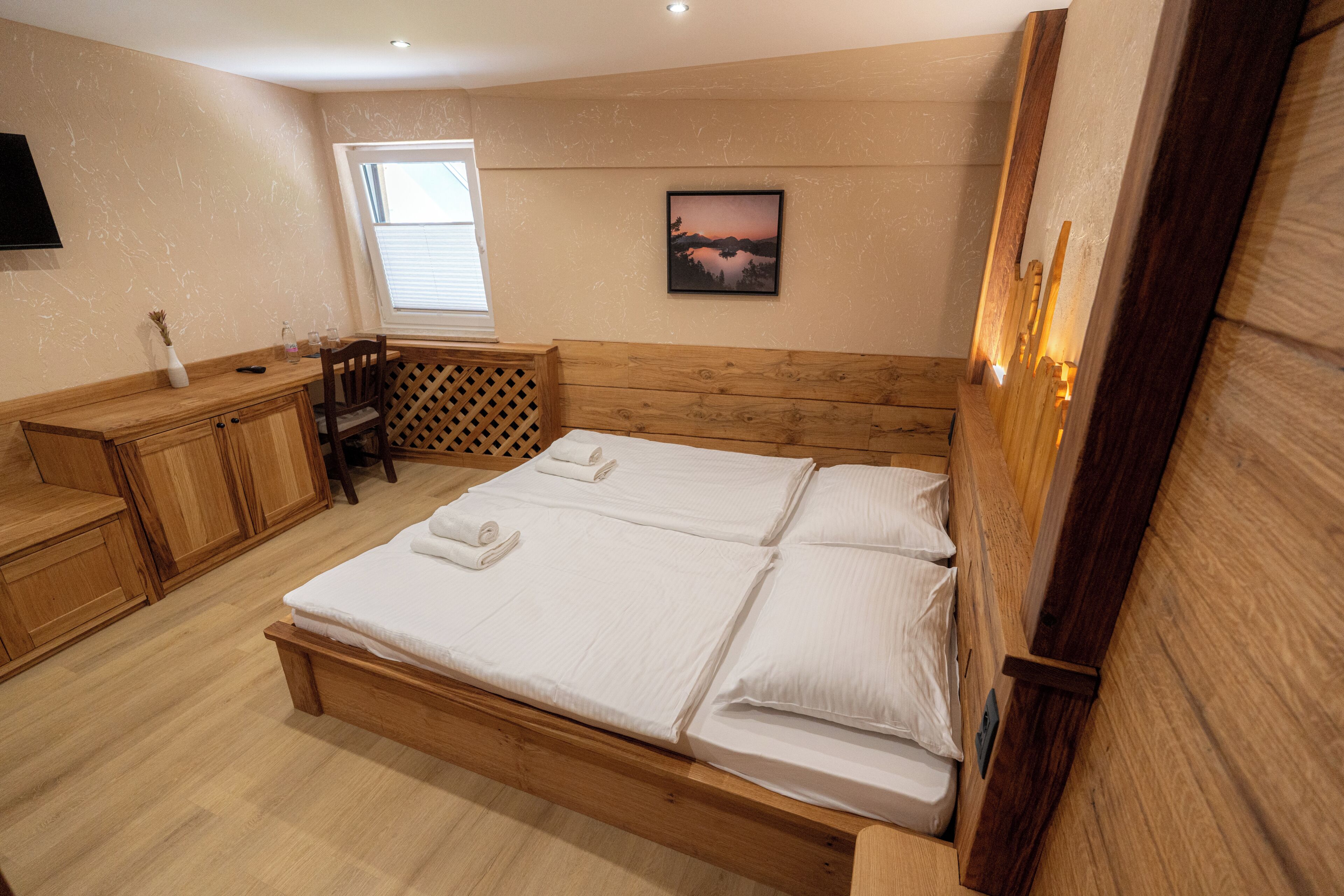 Ein Schlafzimmer mit einem hölzernen Bett, einem Schreibtisch, einem Stuhl, einem Fenster und einem Gemälde an der Wand.