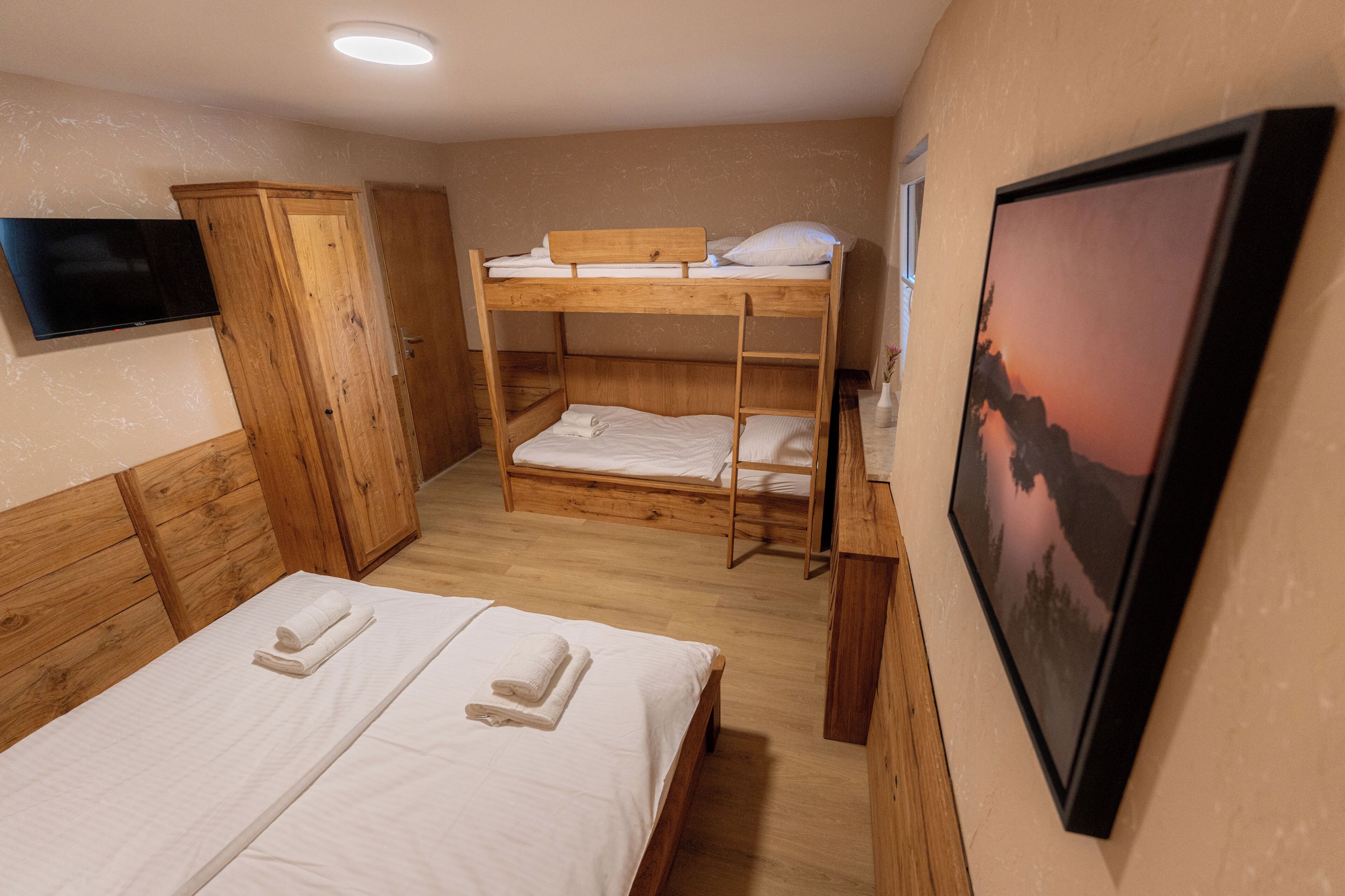 Une chambre avec des lits superposés, une armoire en bois, un téléviseur à écran plat et un tableau encadré au mur.