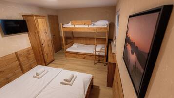 Une chambre avec des lits superposés, une armoire en bois, un téléviseur à écran plat et un tableau encadré au mur.