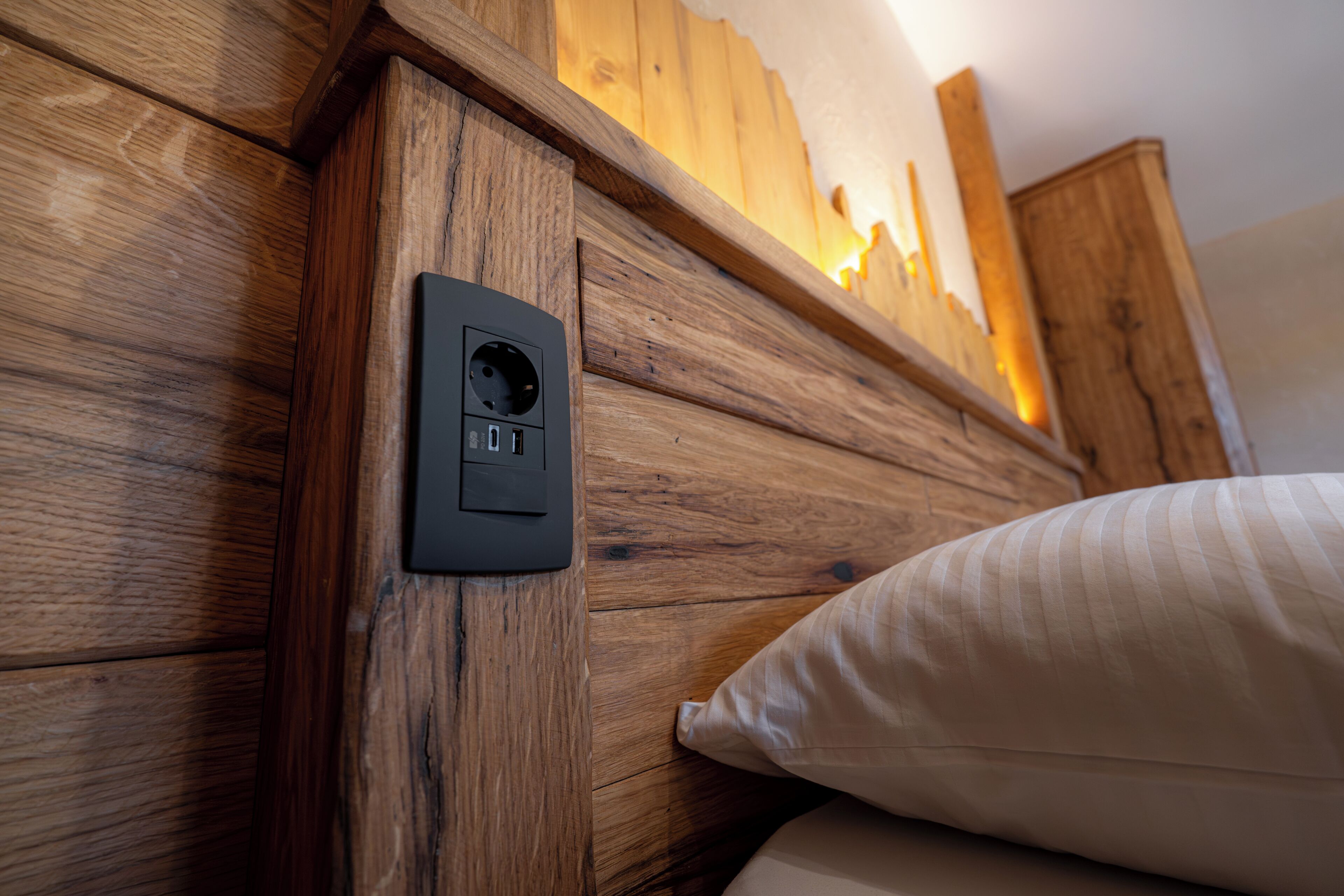 Une tête de lit en bois avec une prise électrique et un oreiller blanc.