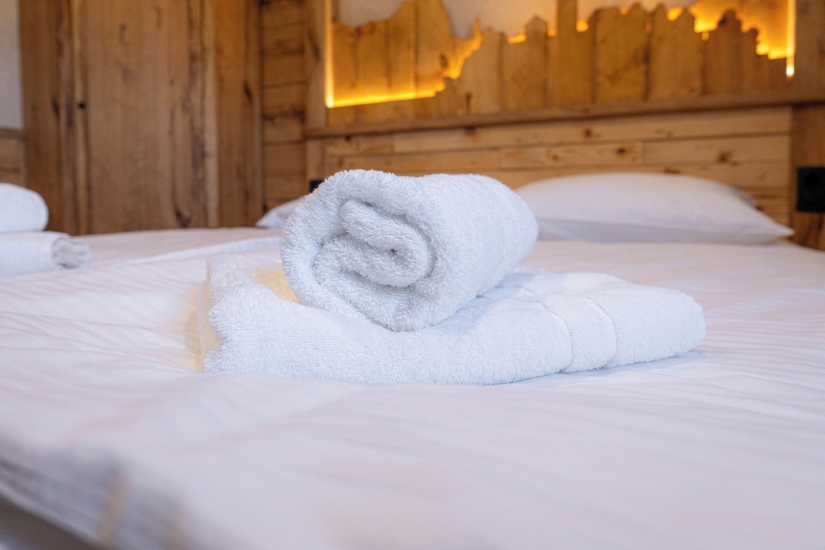 A neatly made bed with a rolled white towel in a room with wooden walls and a cityscape mural.