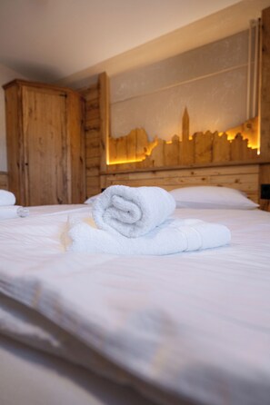 A neatly made bed with a rolled white towel in a room with wooden walls and a cityscape mural. - Bed & Breakfast LakeBled House (Bled)