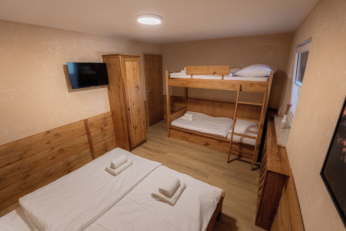 A bunk bed room with a television on the wall, wooden furniture, and a window.