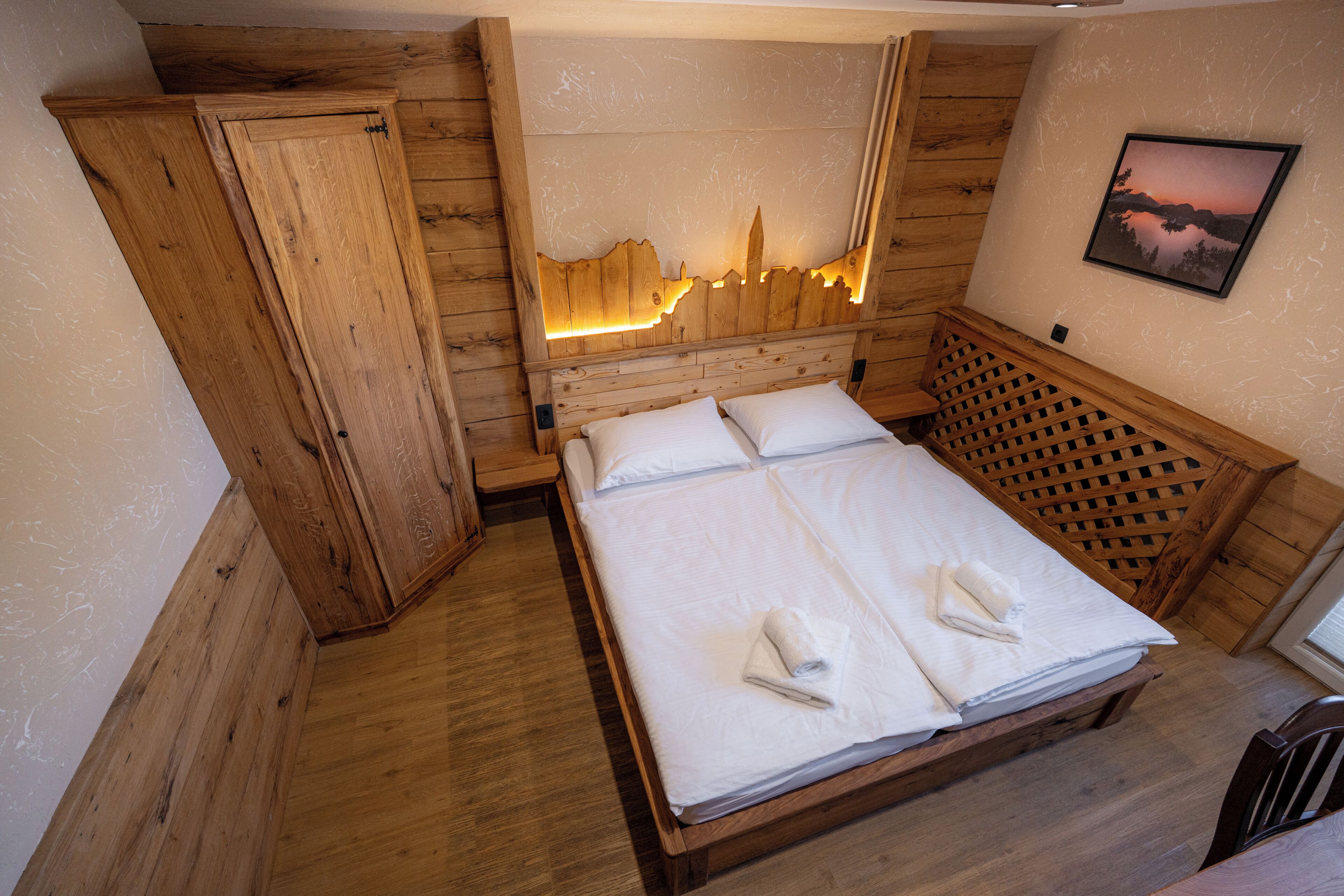 A wooden room with a bed, a wardrobe, and a wall-mounted picture.