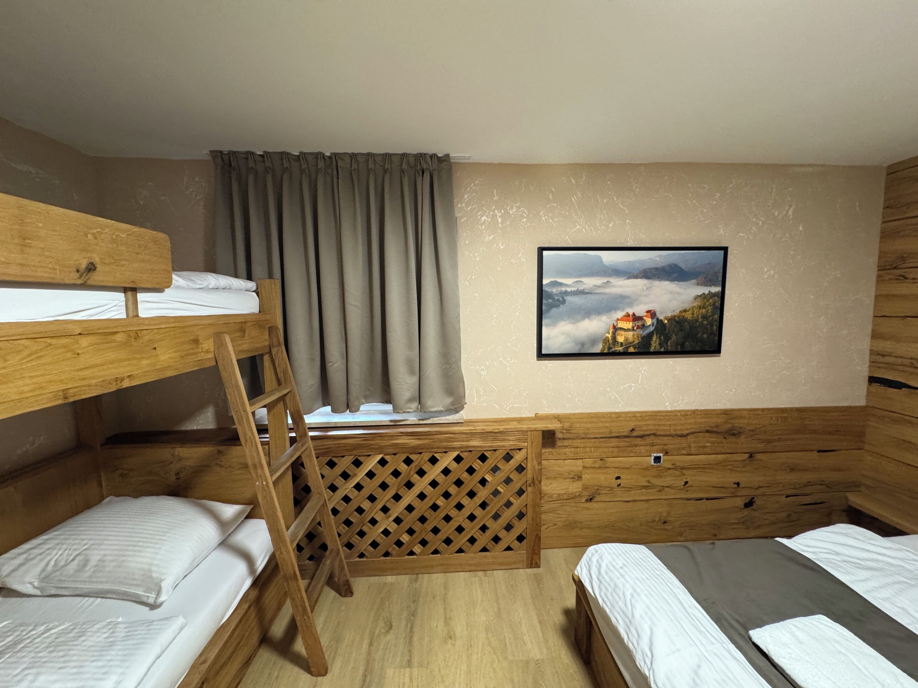 A bunk bed room with a ladder, a window with curtains, and a picture on the wall.