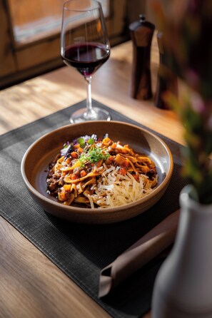 A bowl of pasta with a glass of red wine on a table with a placemat.