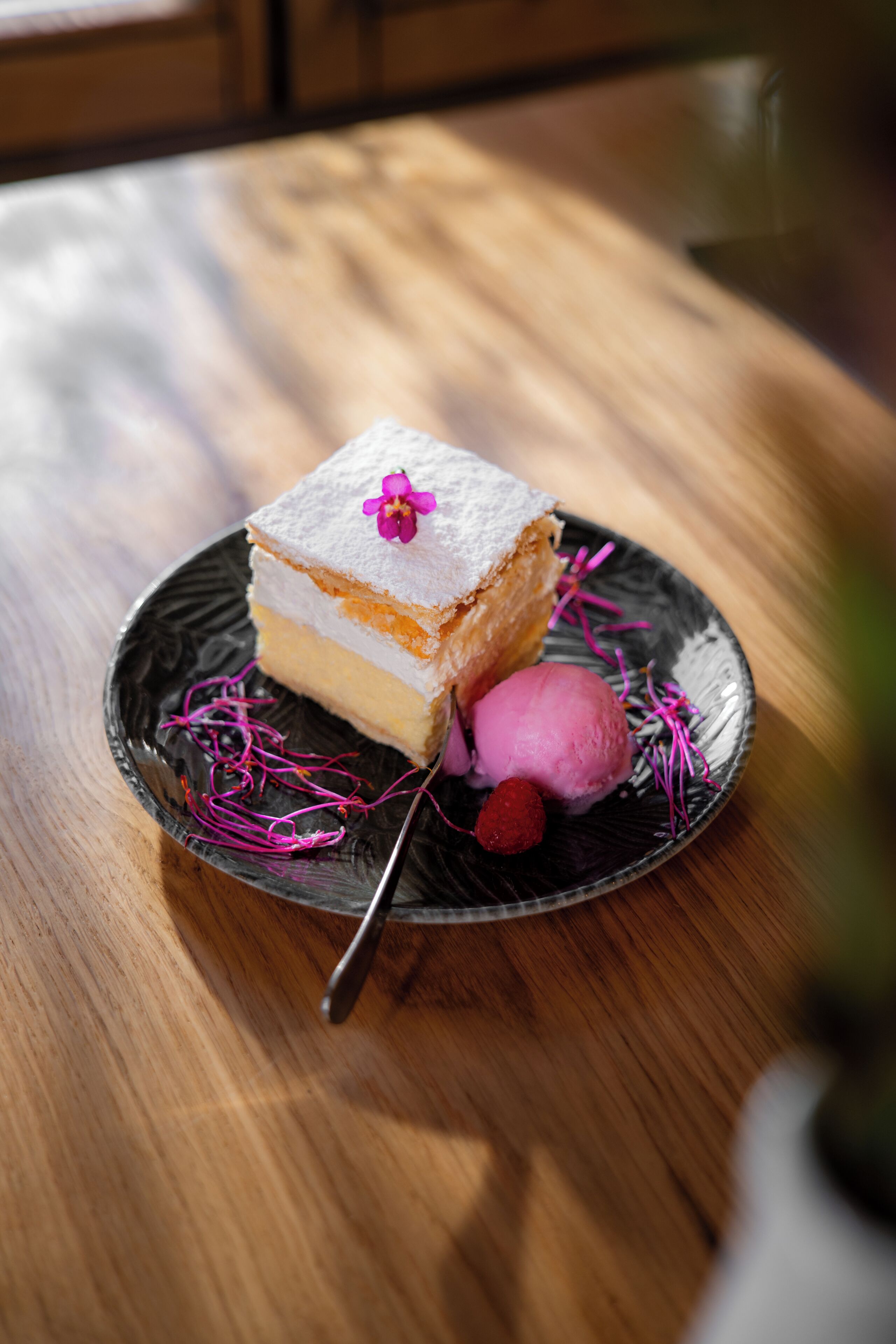 Ein Stück Kuchen mit einer Blume, eine Kugel Eis und eine Himbeere auf einem Teller.