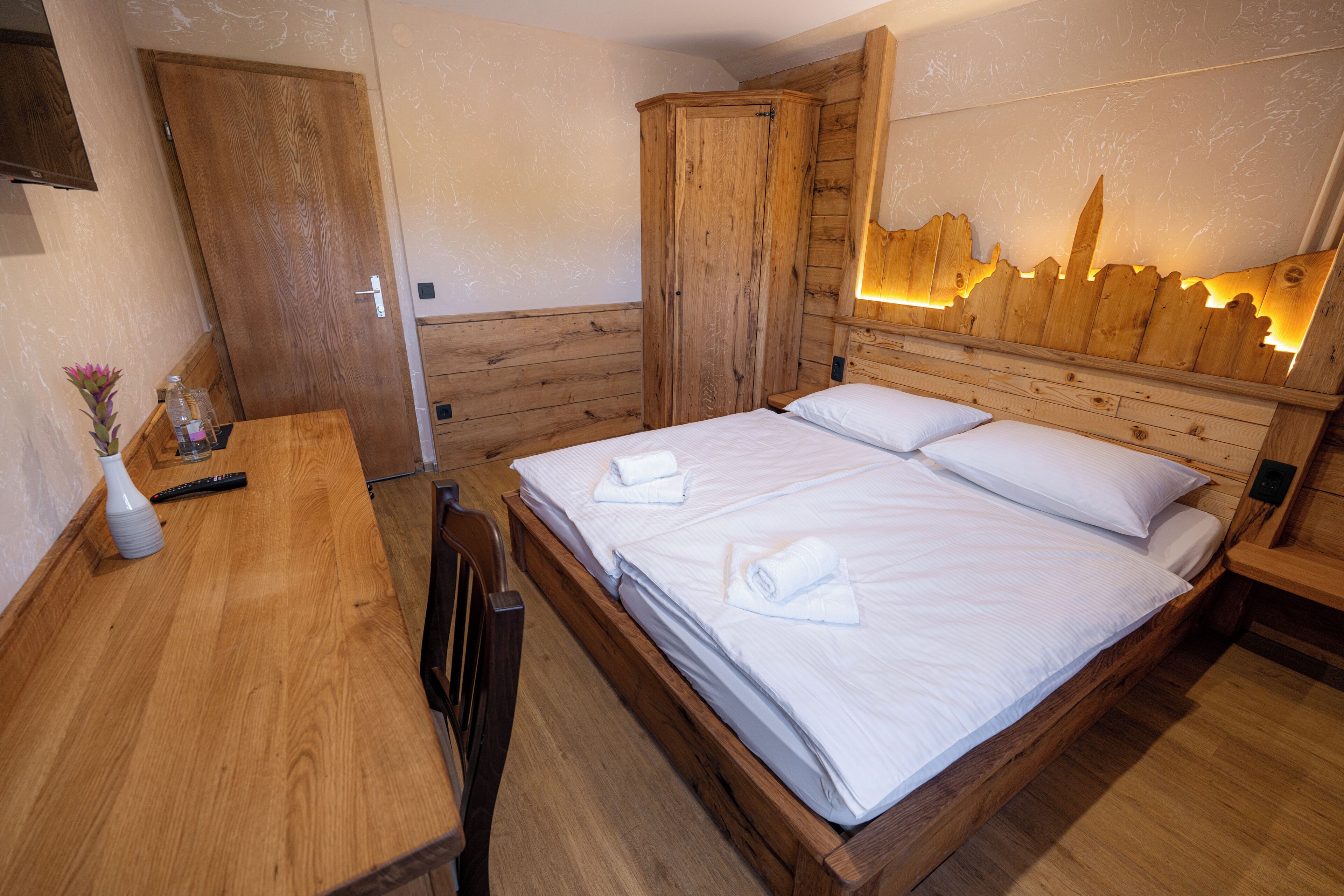 A wooden room with a bed, a desk, and a wardrobe.