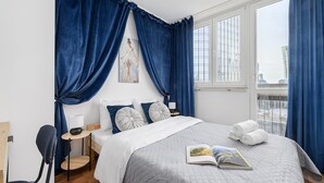 Een moderne hotelkamer met een groot bed, nachtkastje, stoel en een raam met gordijnen.