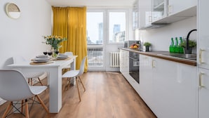 Een moderne keuken met witte kasten, een eettafel met stoelen, en een raam met gele gordijnen.