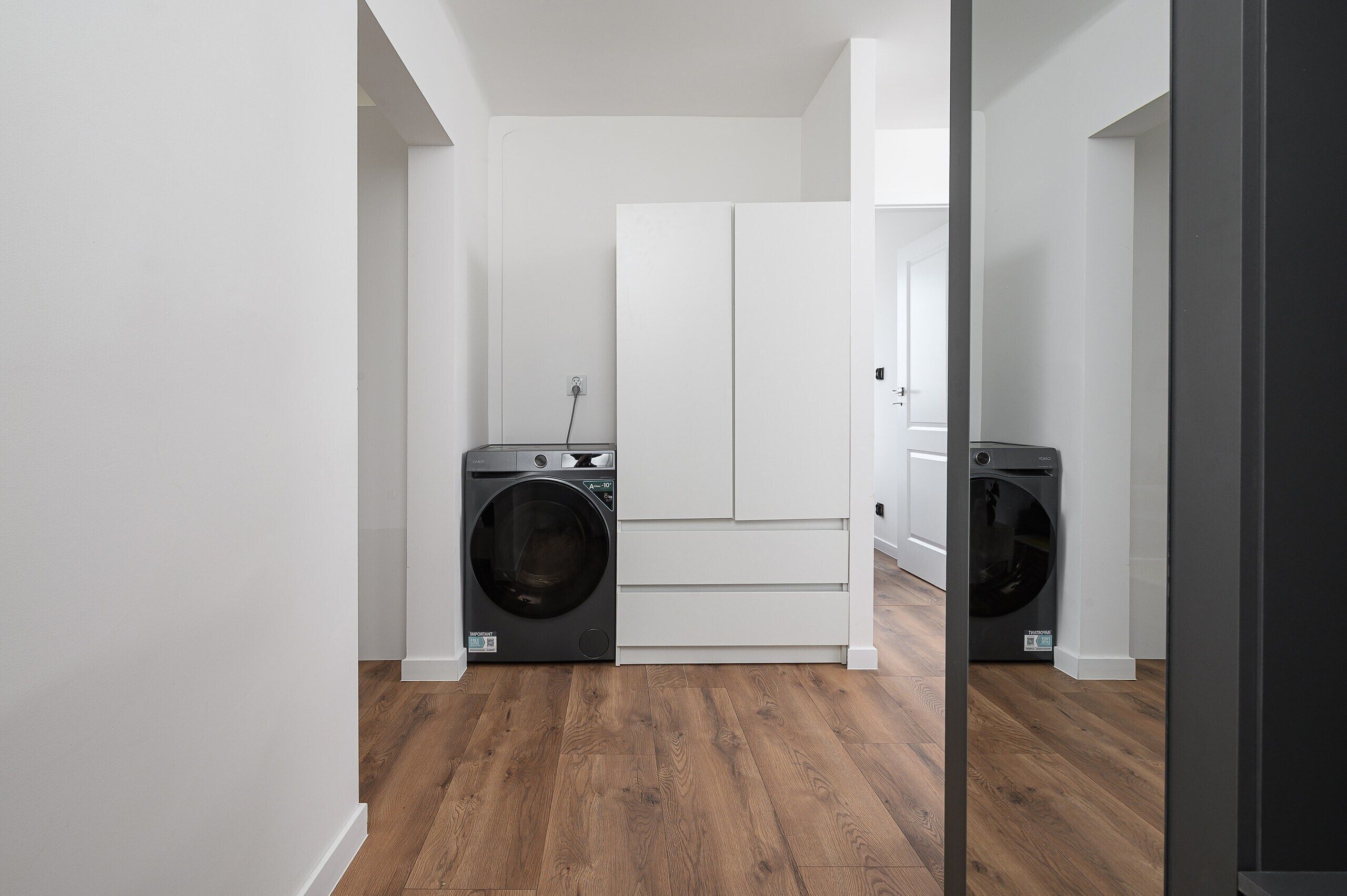 A laundry room with two front-loading washing machines, a white door, and wooden flooring.