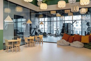 Een moderne sportschool met fitnessapparatuur, grote ramen en een zithoek met zitzakken en kussens.
