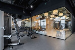 A modern gym with exercise equipment, a weight rack, and a glass wall reflecting the interior. - Modern Apartment | Sauna, Gym and Parking (Katowice)