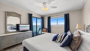 Ein Schlafzimmer mit Bett, Fernseher, Deckenventilator, Kommode und Meerblick.