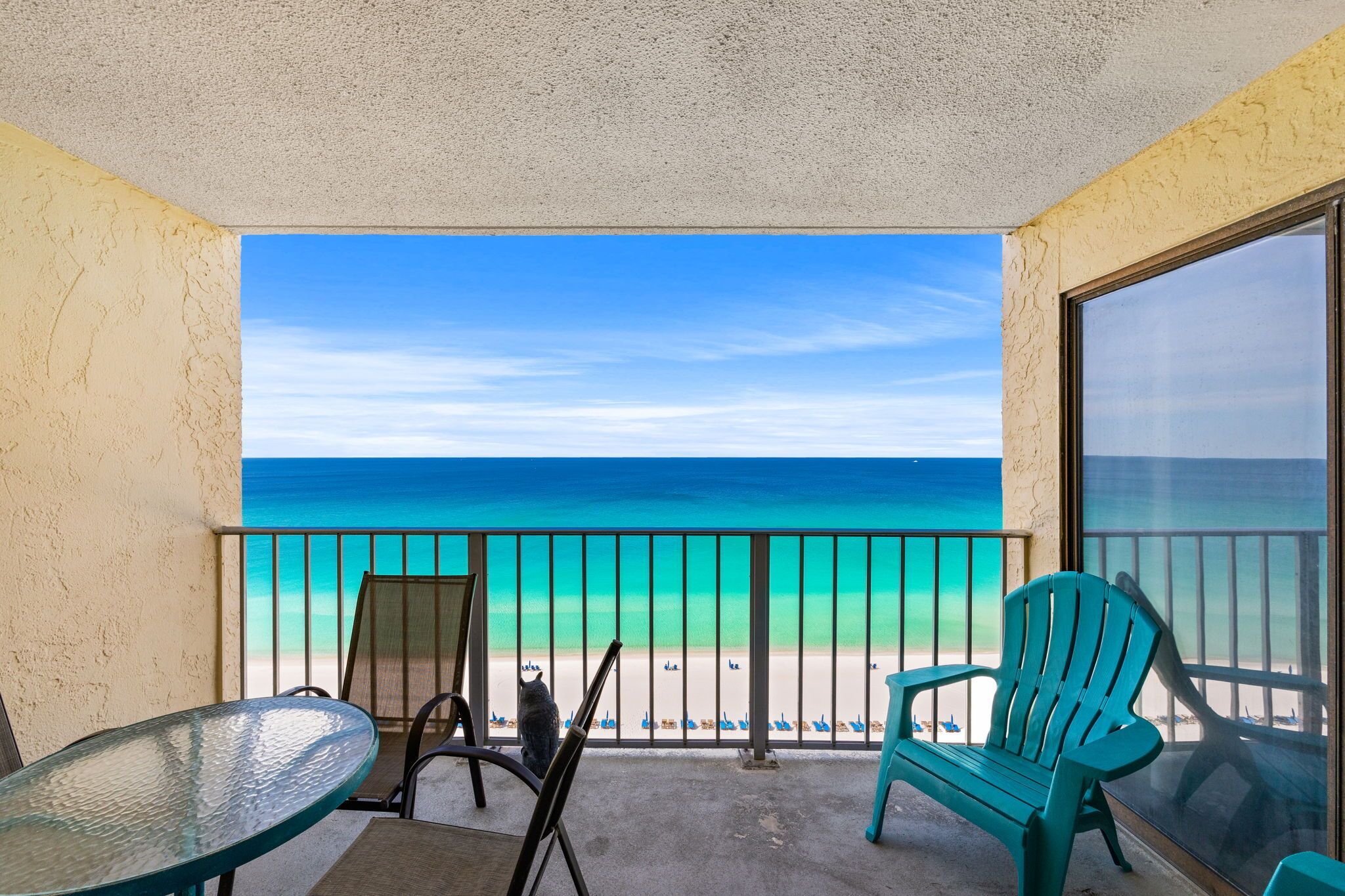 A balcony with a view of the beach, a glass table, two chairs, and a large window.