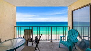 Ein Balkon mit Blick auf den Strand, einem Glastisch, zwei Stühlen und einem großen Fenster.