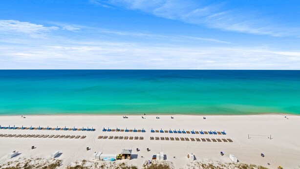 Ein Strand mit Reihen blauer Sonnenschirme und weißer Zelte, einem klaren, blauen Himmel und einem ruhigen Meer.