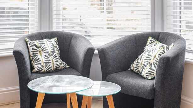Two grey armchairs with leaf-patterned cushions and a small glass table with wooden legs. - Host & Stay | Elmville (Scarborough)